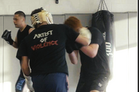 Two individuals in a martial arts training session with one wearing a 'Artist of Violence' shirt.